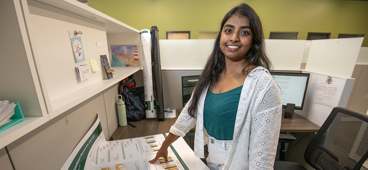A woman smiles behind a desk with her hand on a research poster