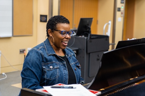 A female faculty member in a jean jacket is standing behind a computer on a podium