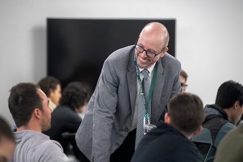 A male faculty member stands against a whiteboard during a lecture
