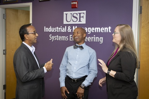 A group of three faculty members standing together and chatting
